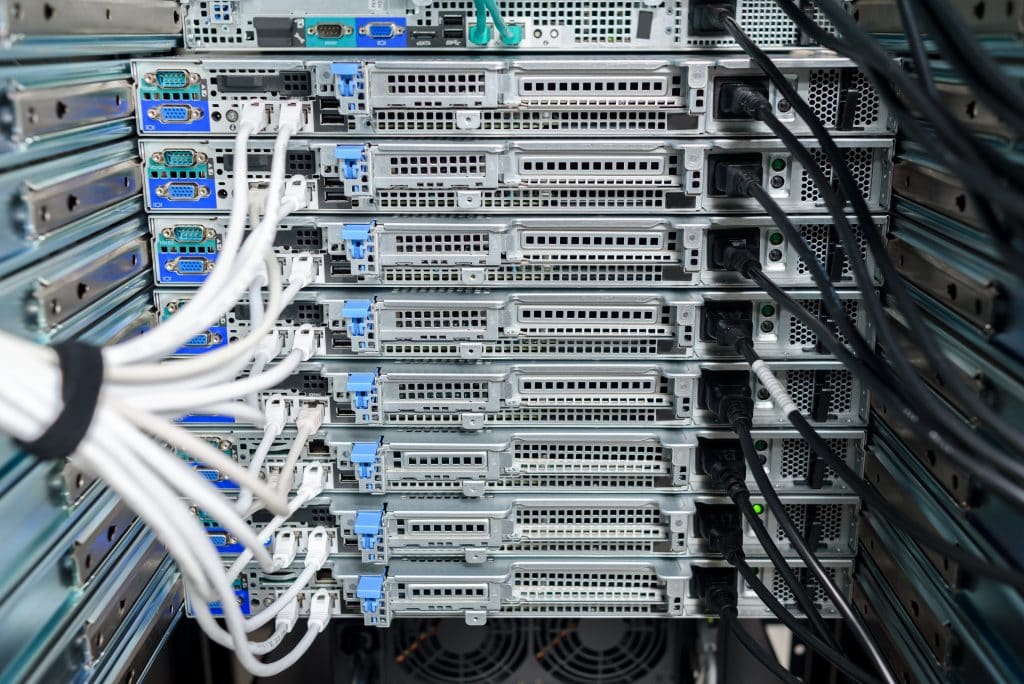 A close-up view of stacked server units in a server rack, showing various ports at the back and multiple cables connecting them.